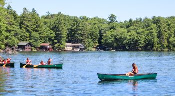Campers canoe near shoreline with cabins behind them