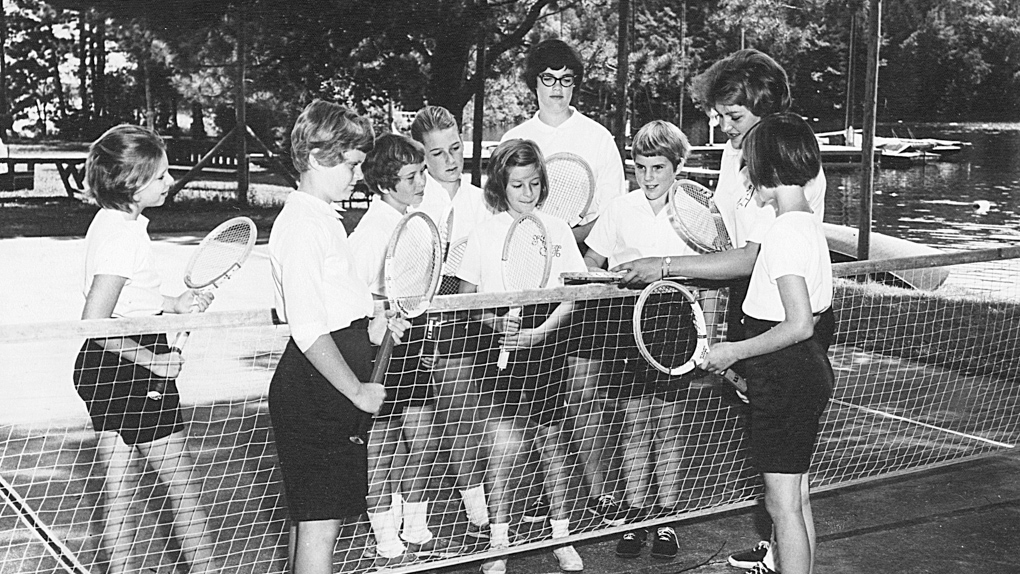 1962 photo of campers gathered around net on tennis court