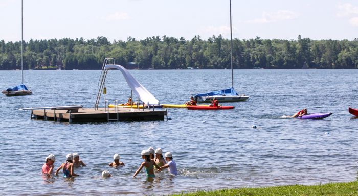 Campers swim in waterfront area in front of floating dock and boats