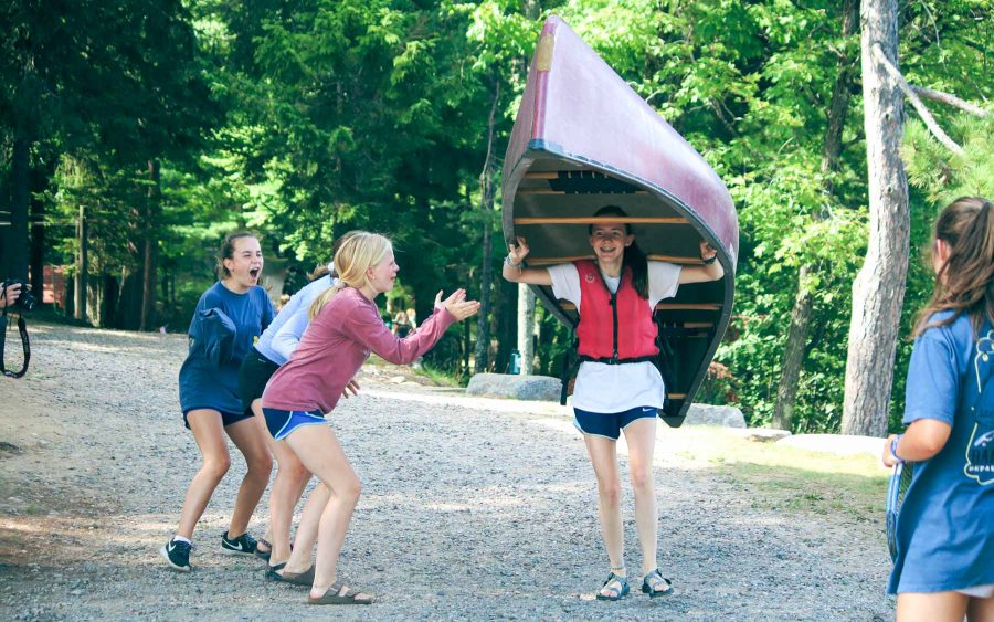 Camper carrying canoe while others cheer