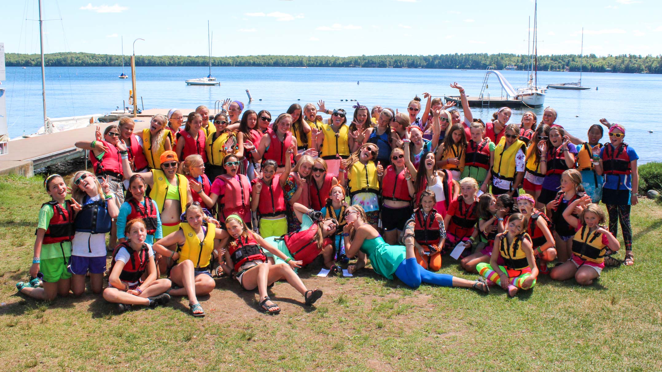 Group of campers pose in front of waterfront in life jackets