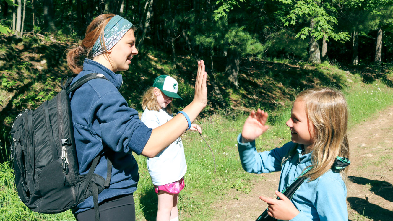 Camp staff member high fives young camper