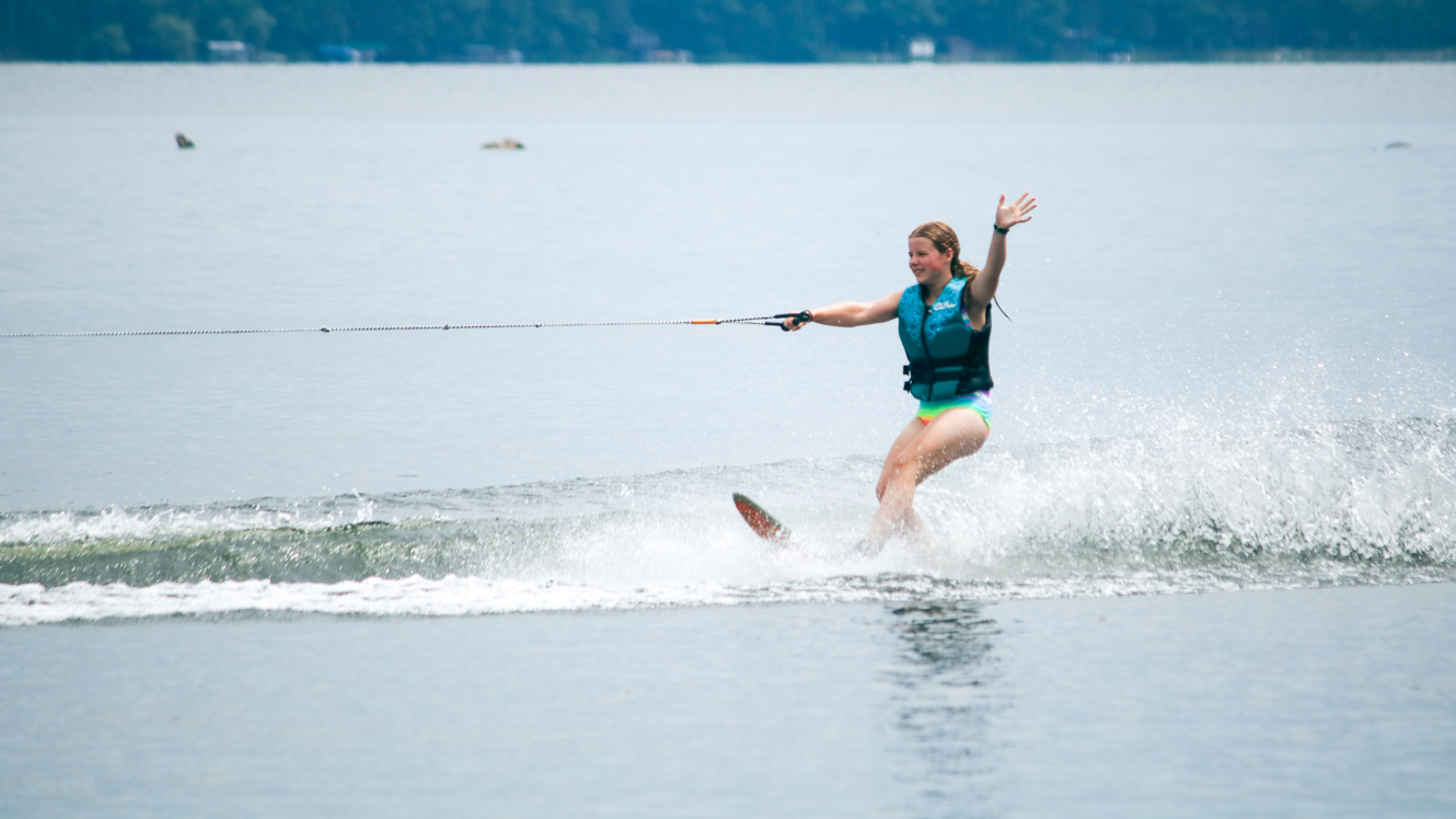 Girl waves while water skiing at summer camp