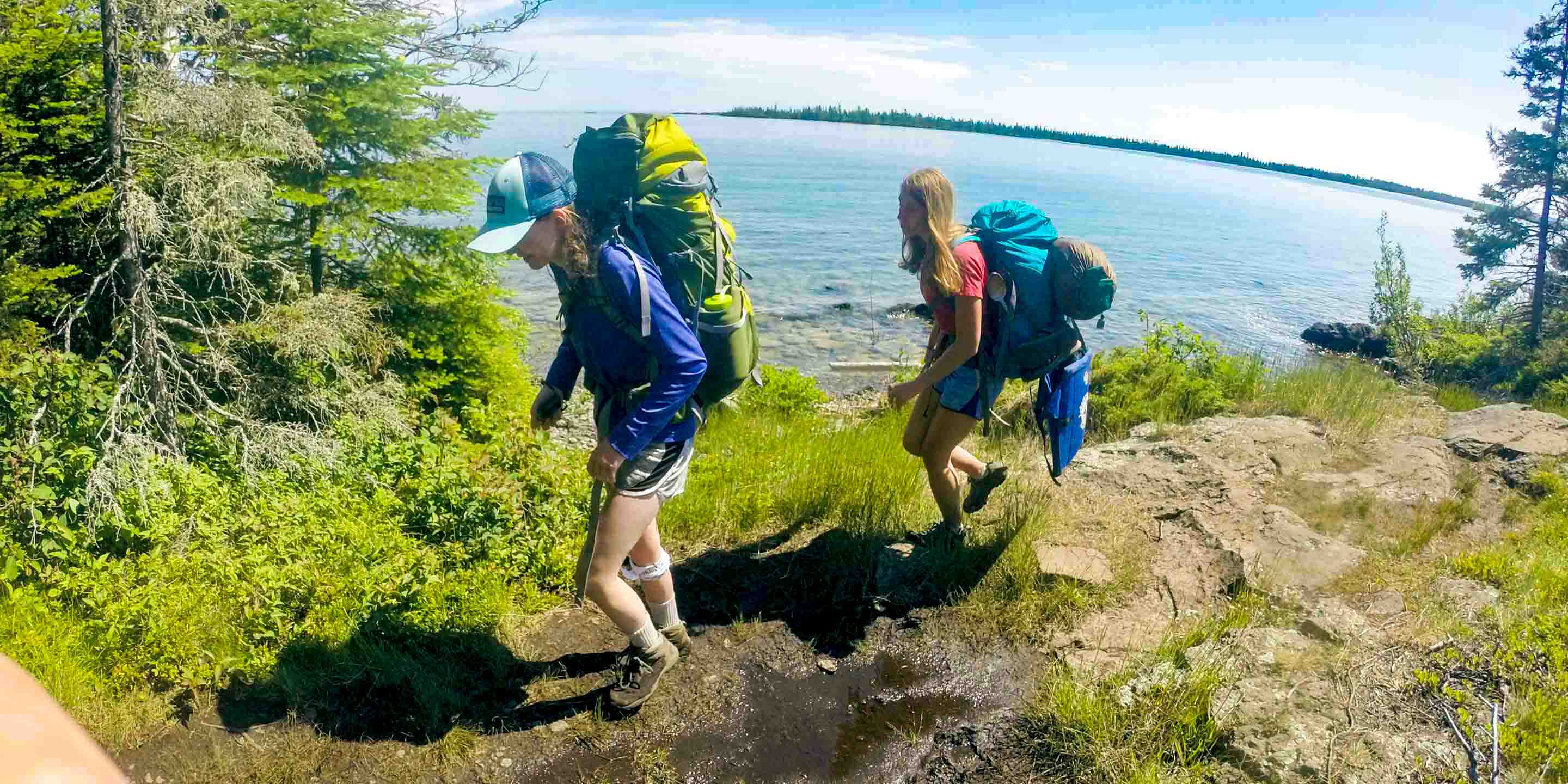 Girls backpack along lakeshore during camp trip