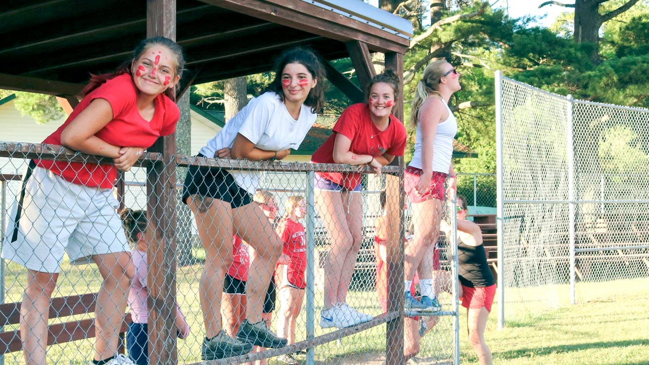 Campers stand on fence to watch sports game