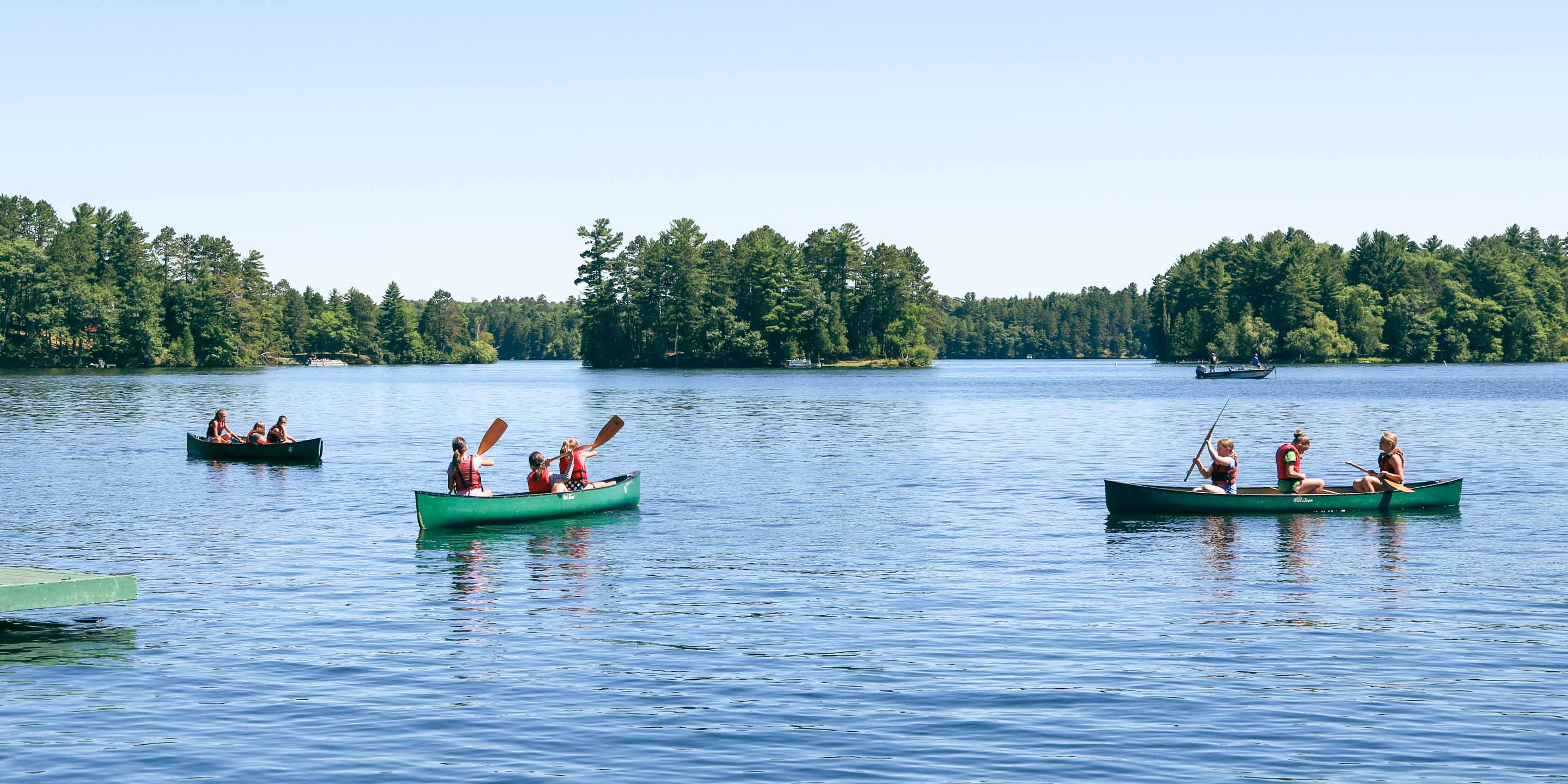Three canoes carrying campers across the lake