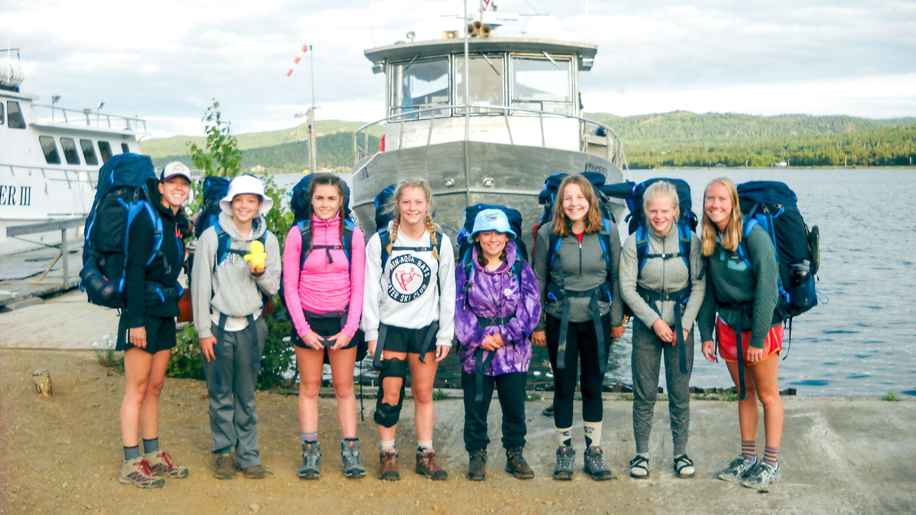 Group stands in front of boat on camp trip