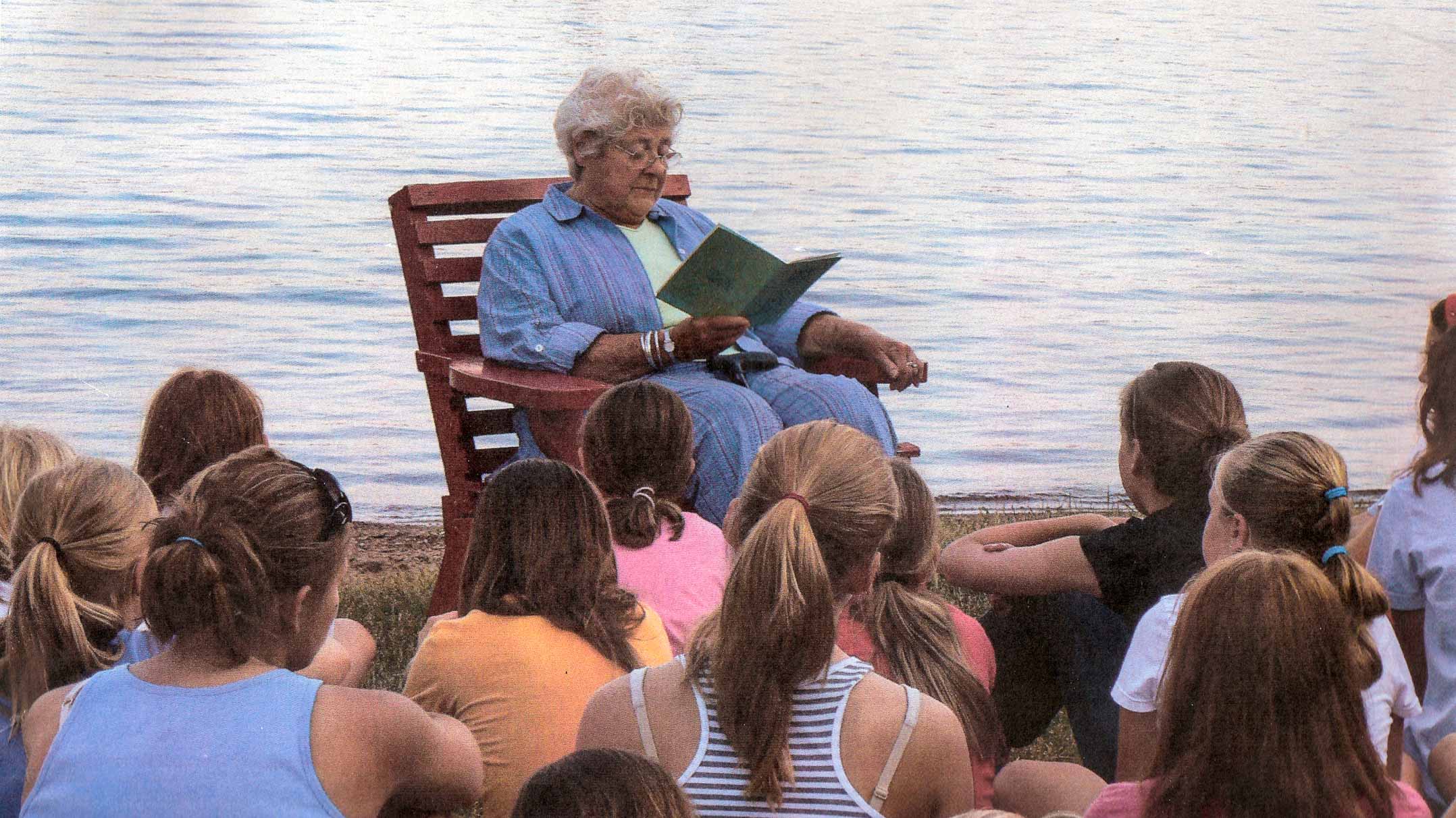 Sunny reads to campers by lakeshore